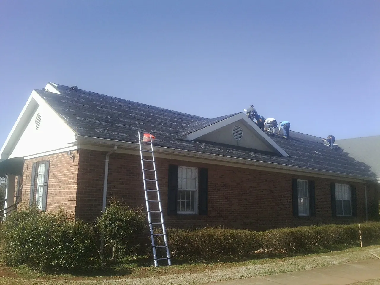 Crew tearing shingles off a brick ranch roof with a ladder set — Metal Roof Repair work by our crew in Edwards